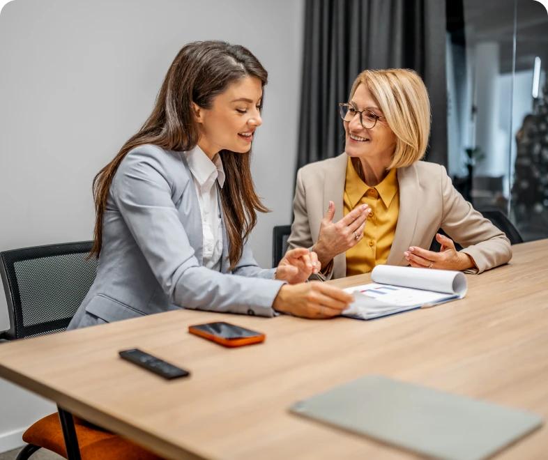 Two women discussing papers at desk.