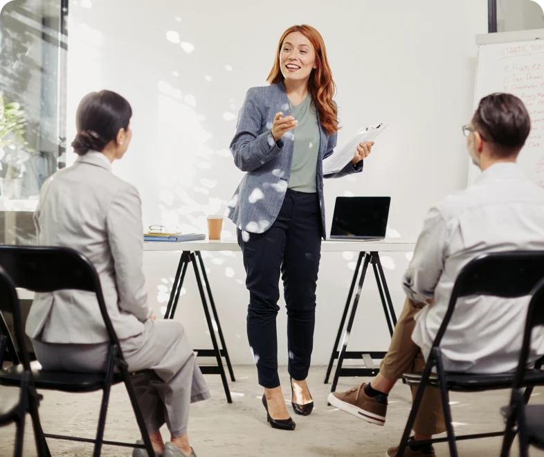 Woman presenting to seated colleagues in office.